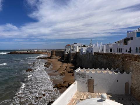 Whitewashed seaside ramparts and crashing surf along sandy beach under dramatic sky.