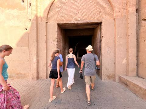 Travellers walk through a tall arched entrance of an old Moroccan structure.