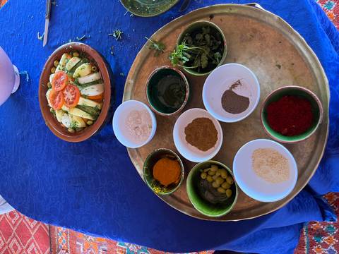 Assortment of Moroccan spices and herbs in small bowls beside a fresh vegetable salad