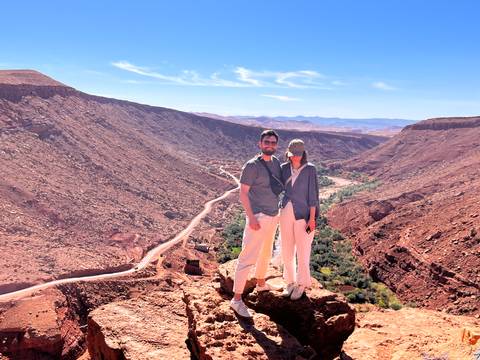 Couple posing on ridge overlooking dramatic red canyon with green river oasis below