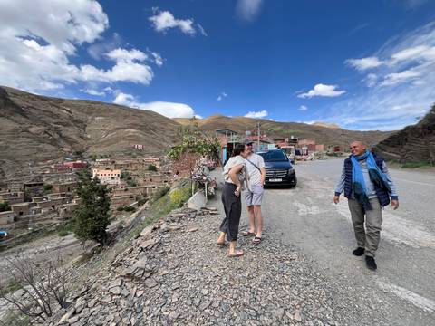 Travellers chatting beside van on roadside overlooking remote mountain village