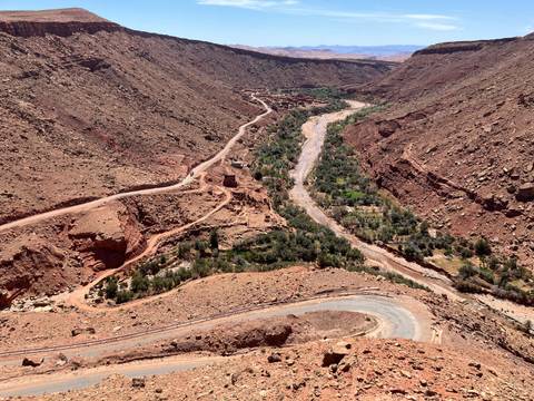 Aerial perspective of winding road and river through steep red canyon in Morocco
