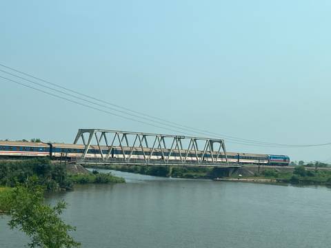 Long passenger train crossing a steel truss bridge over a wide river.