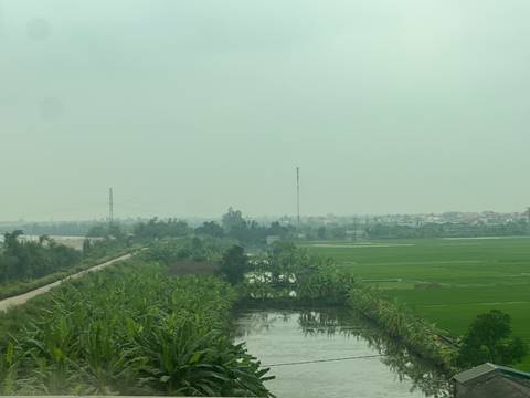 Wide view of hazy green rice fields, canals, and distant villages.