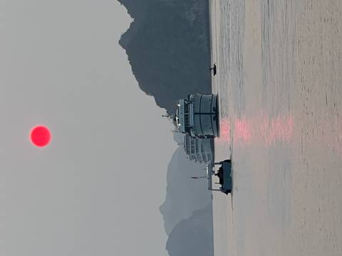 Cruise ships gliding through the calm waters of Ha Long Bay at sunset with a vivid red sun.