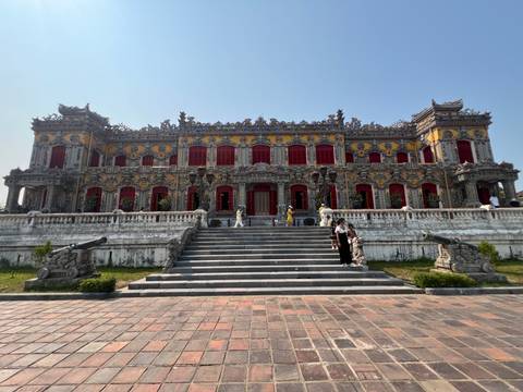 Ornate yellow building with red shutters and cannons, visitors on the grand staircase.