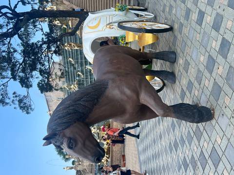 Life-size brown horse statue hitched to a decorative carriage in a public square.