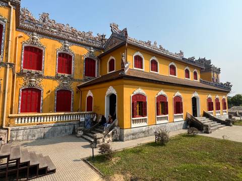 Yellow imperial residence with ornate roof and bright red shutters within Hue's citadel.