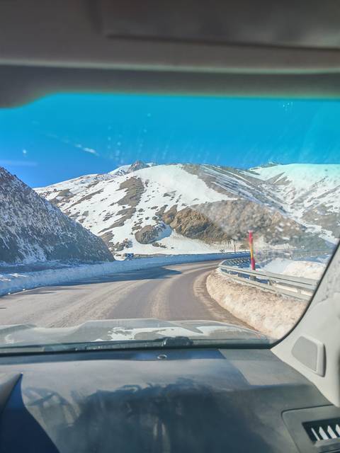 Snow-lined mountain pass road viewed through vehicle windshield with blue sky