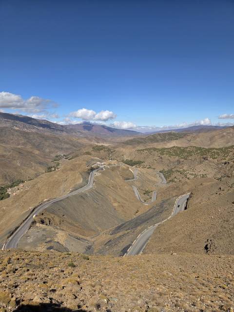 Aerial view of winding mountain road cutting through arid brown ridges under scattered clouds