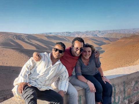 Travel companions posing arm-in-arm on a viewpoint overlooking rolling desert hills in Morocco