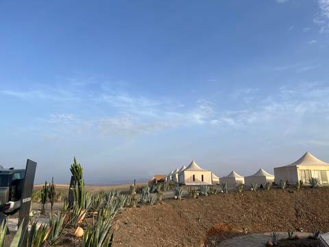 Row of luxury canvas tents and cacti on a barren desert ridge under a pale blue sky