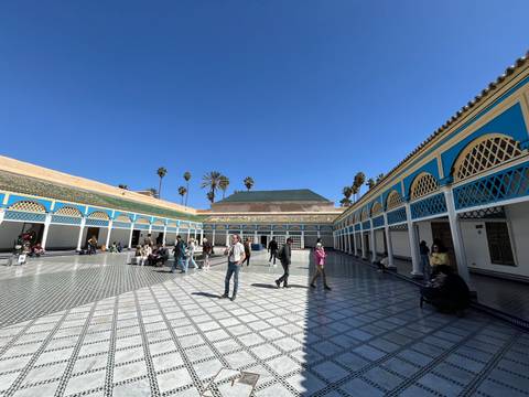 Vibrant tiled courtyard of Bahia Palace with tourists walking and blue-and-yellow arches framing the space