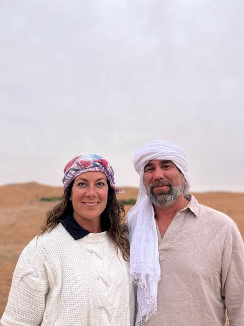 Portrait of couple wearing traditional scarves with soft desert landscape blurred behind.