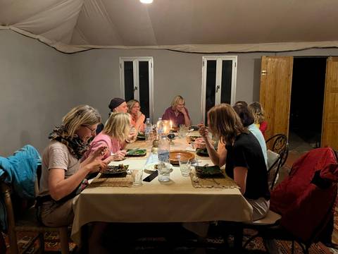 Travellers share an evening meal around a candle-lit table inside a desert camp dining tent.