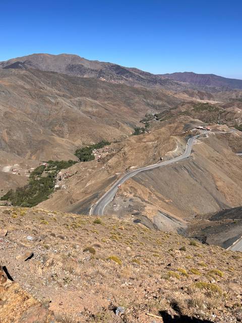 A serpentine mountain road winds through barren brown slopes with tiny villages nestled in valleys.