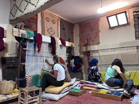 Women weave colourful carpets on vertical looms inside a traditional Moroccan workshop.