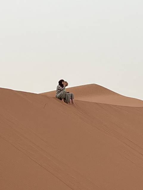 Romantic couple sits on the crest of an orange sand dune sharing a quiet kiss.