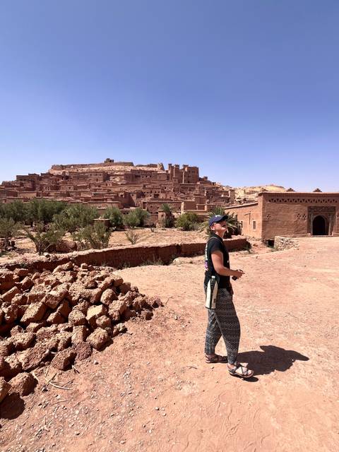 Traveller looks up at the earthen citadel of Ait Benhaddou from a sun-baked courtyard.