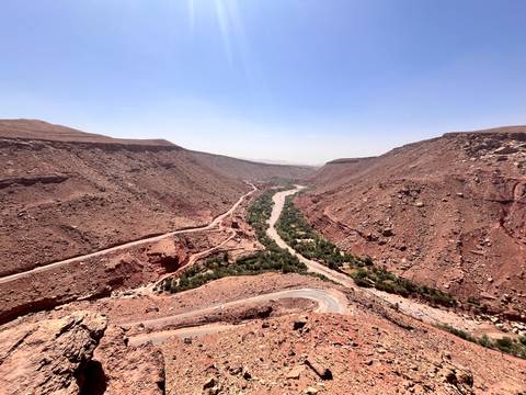 Sweeping canyon view with a river snaking through arid red cliffs and winding mountain road.