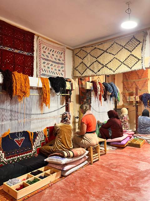 Artisans working at colourful rug looms in a lively Moroccan weaving cooperative.