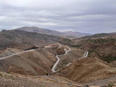 Sweeping mountain panorama with a serpentine highway snaking through barren ridges under a cloudy sky.