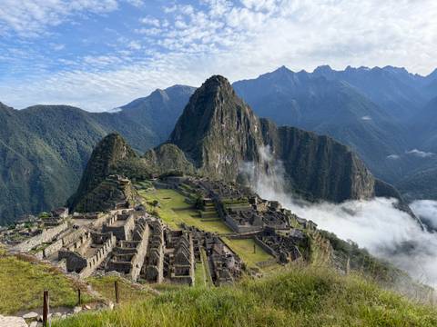 Iconic panoramic view of Machu Picchu ruins perched on a ridge with Huayna Picchu peak and drifting clouds behind.