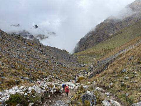 Trekkers ascend a rocky high-altitude pass shrouded in mist between steep slopes.