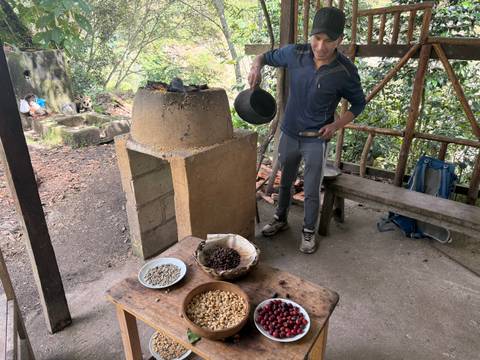 Guide roasts coffee beans over an adobe stove with bowls of raw and roasted beans on a rustic table.