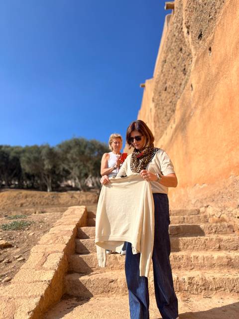 Two women adjusting a scarf near ochre-coloured ancient walls on a bright sunny day.