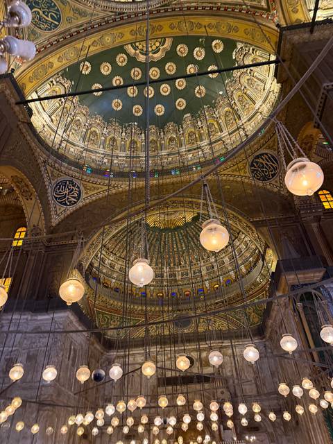 Ornate gilded interior dome of a grand mosque with Arabic calligraphy and hanging lamps.