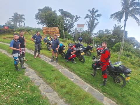 Motorbike riders in full gear pause at a mountain viewpoint beside their dual-sport bikes.