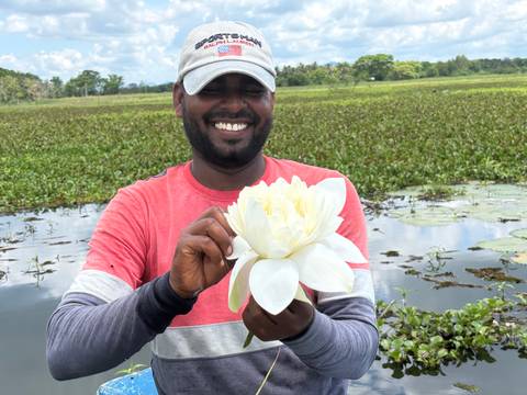 Smiling guide holds a large white lotus flower in front of a lush wetland.