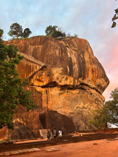 Golden evening light bathes the sheer rock face and stairway of iconic Sigiriya Rock.