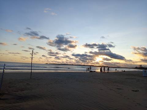 Silhouettes of beachgoers enjoy sunset on a wide sandy shore under cloud-streaked skies.