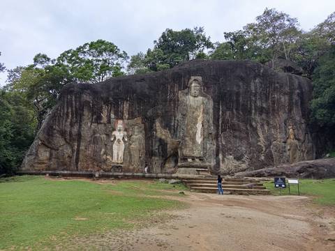 Ancient rock relief statues carved into a massive dark cliff with visitors at the base.