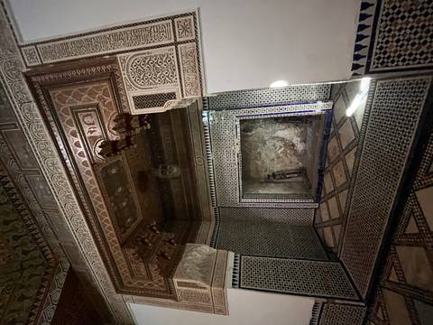 Dimly lit decorated chamber with intricate zellij tilework and carved ceiling inside a Moroccan palace.