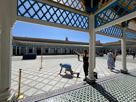 Wide courtyard of Bahia Palace with patterned tiles; tourists explore while one person kneels playfully for a photo.