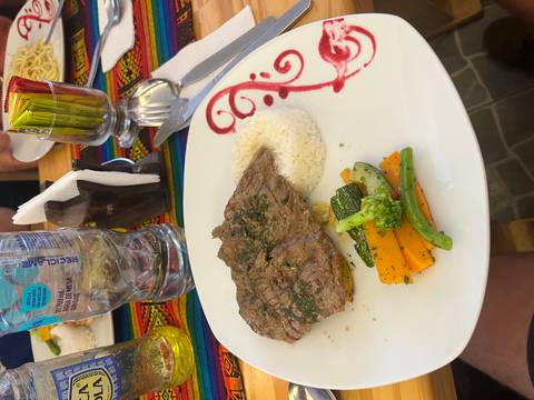 Plate of grilled steak, rice and sautéed vegetables served on colorful Andean textile.