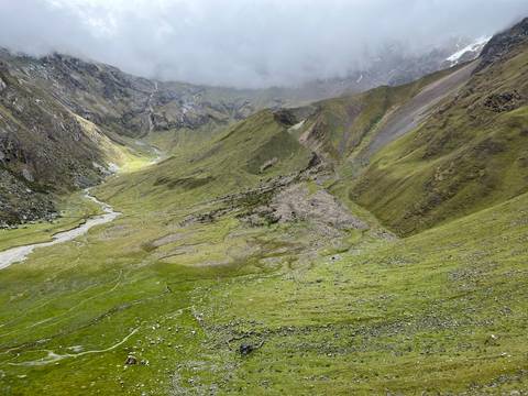 High-altitude green valley and meandering stream under swirling mountain mist on the Salkantay trek.