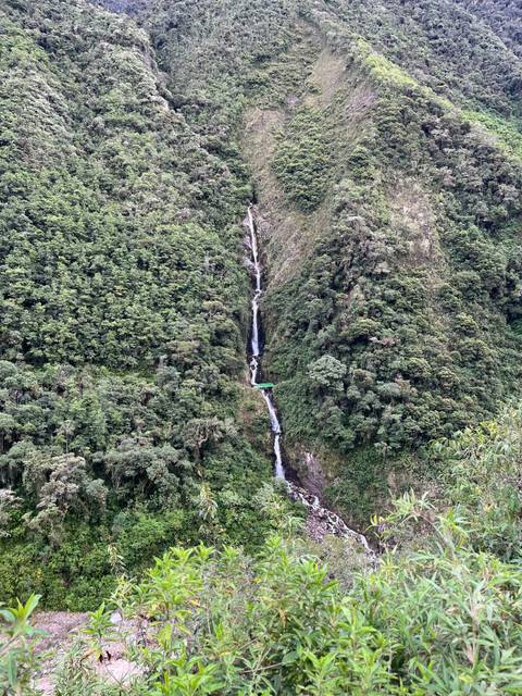 Tall slender waterfall cuts through dense green jungle hillside in Peru.