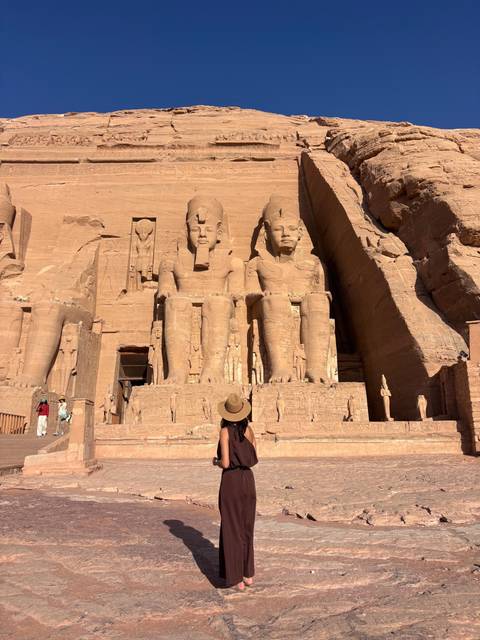 Traveller in sunhat admires the colossal statues of Ramesses II at Abu Simbel temple façade.