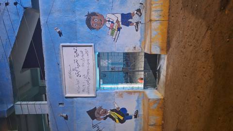 Blue-painted building at night featuring playful murals of schoolchildren and an Arabic sign.