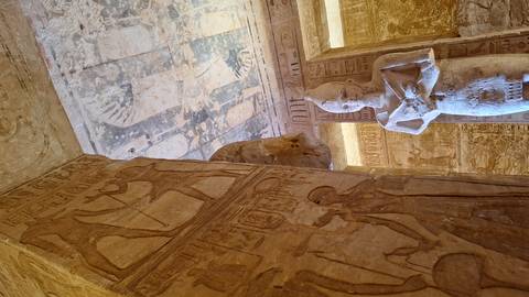 Interior of an ancient Egyptian temple with standing statue and richly carved walls and ceiling.