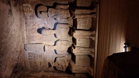 Dim chamber with four seated sandstone statues illuminated by a spotlight in Abu Simbel’s interior.