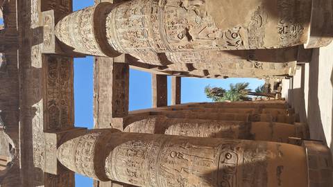 Massive hieroglyph-covered sandstone columns forming a grand colonnade at Karnak Temple under blue sky.
