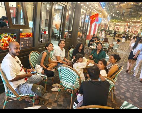 Multi-generational family relaxing around café tables at an indoor food street lined with colourful décor.