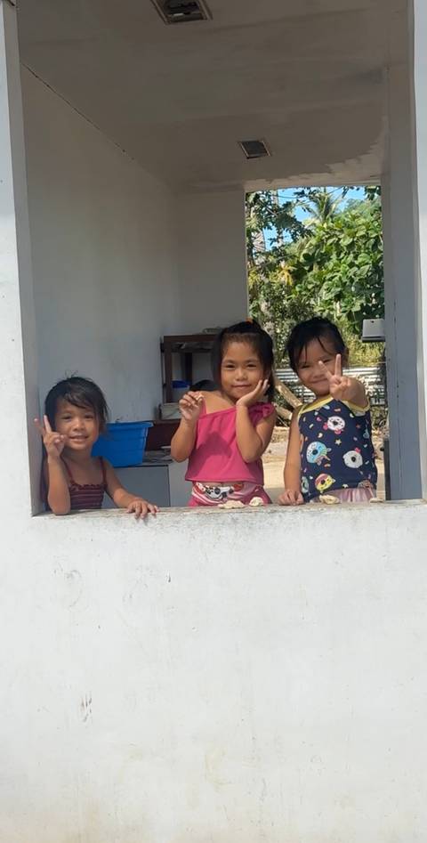 Three smiling young girls flashing peace signs while leaning on a white windowsill