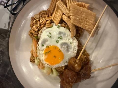Close-up of a plated Asian rice dish topped with a sunny-side egg, skewered meats, peanuts and crackers.