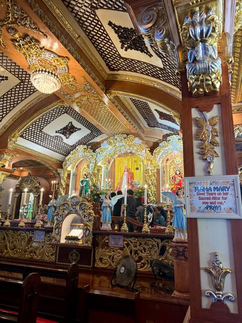 Lavish, gold-trimmed Catholic altar filled with statues, candles and worshippers inside an ornate church.